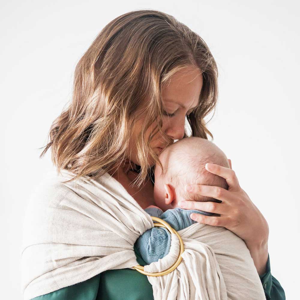 New Season Doula Care carrying a baby in a sling and kissing its forehead