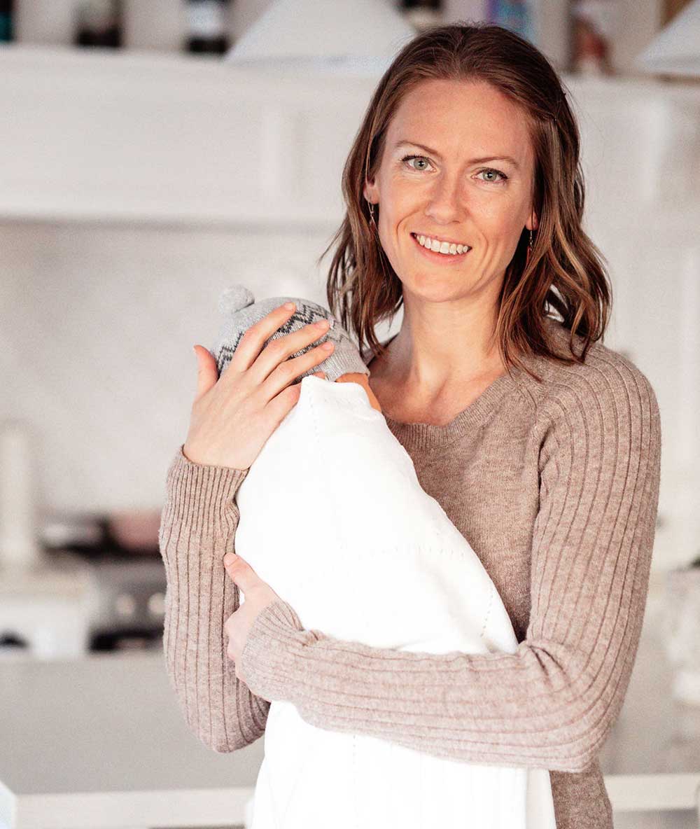 New Season Doula in Melbourne standing in kitchen holding a baby wrapped in a blanket
