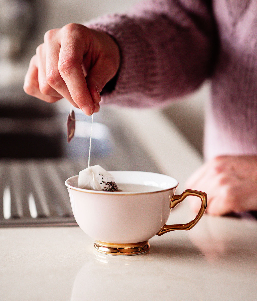 A hand holding a teabag in a cup of tea