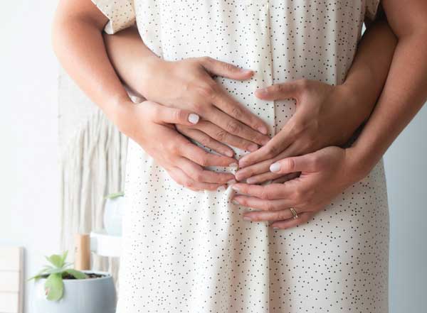 Close up image of a pregnant belly with hands holding the belly