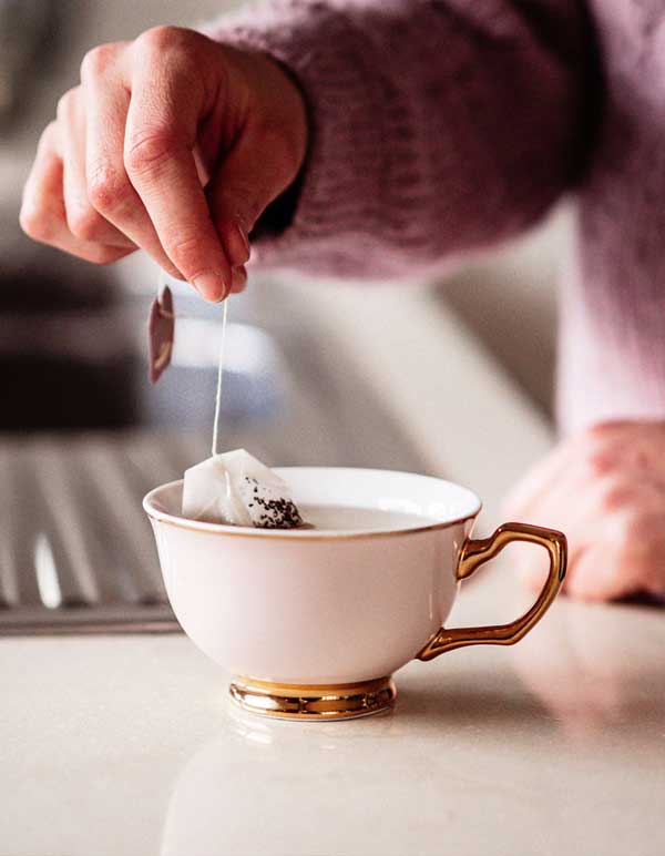Hand holding a teabag in cup of tea